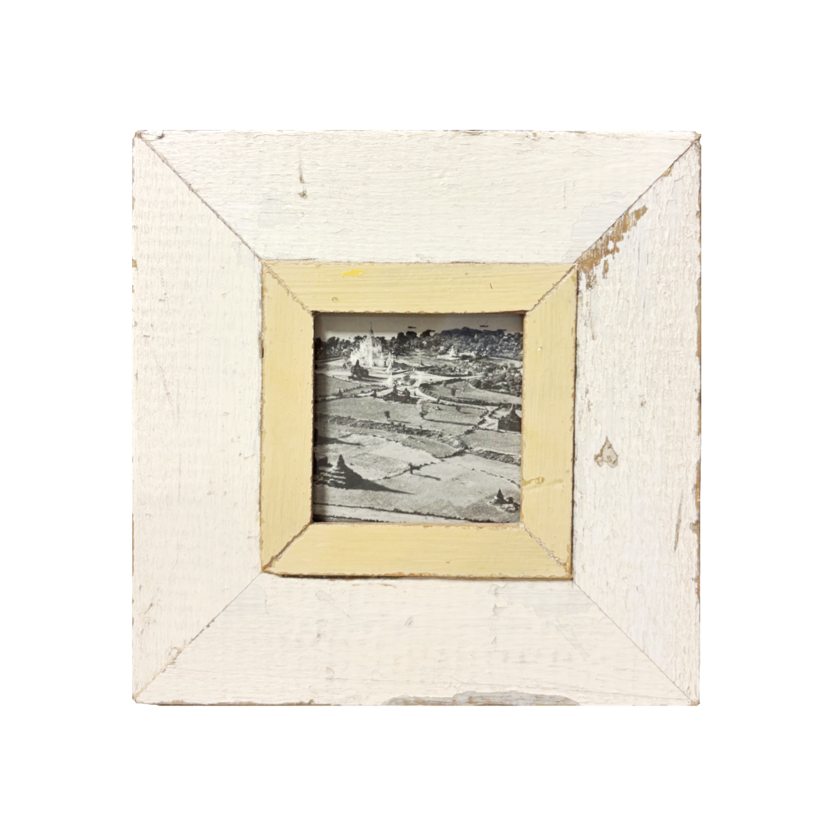 Cornice quadrata bianco antico 23×23 cm con passe-partout giallo pallido consumato, contenente fotografia analogica B&W di paesaggio agricolo con ombre lunghe diagonali e castello luminoso sullo sfondo, stile Mid-Century Modern, legno recuperato Cape Town