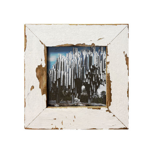 Opera Industrial "La Foresta d'Acciaio": cornice 23×23 cm in legno recuperato bianco con vernice scrostata, fotografia a colori di tubi cilindrici argentati su sfondo di alberi e cielo