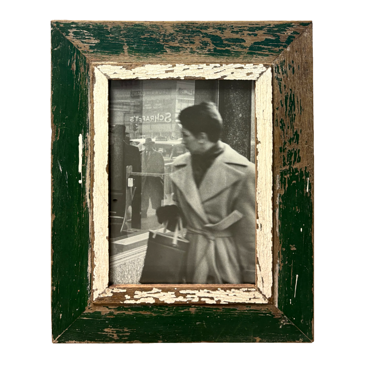  Cornice rettangolare verde imperiale 34×43 cm con passe-partout in legno bianco/crema e scrostature marroni naturali sui bordi, contenente fotografia B&W documentaria di donna in abito invernale chiaro che osserva distrattamente una vetrina storicamente segnata (insegna SCHRAFT'S), traffico e passanti riflessi nel vetro, stile Classico metropolitano, legno recuperato Cape Town, aria metropolitana mid-century 