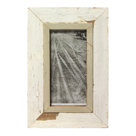 Fotografia minimalista in bianco e nero di tracce di pneumatici su strada fangosa, racchiusa in cornice di legno bianco sporco scrostato con passe-partout greige, stile minimalista.